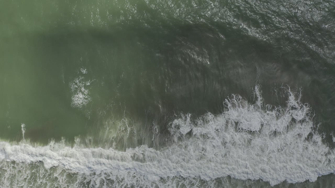Overhead ocean frame with a foamy wave band moving across green water.