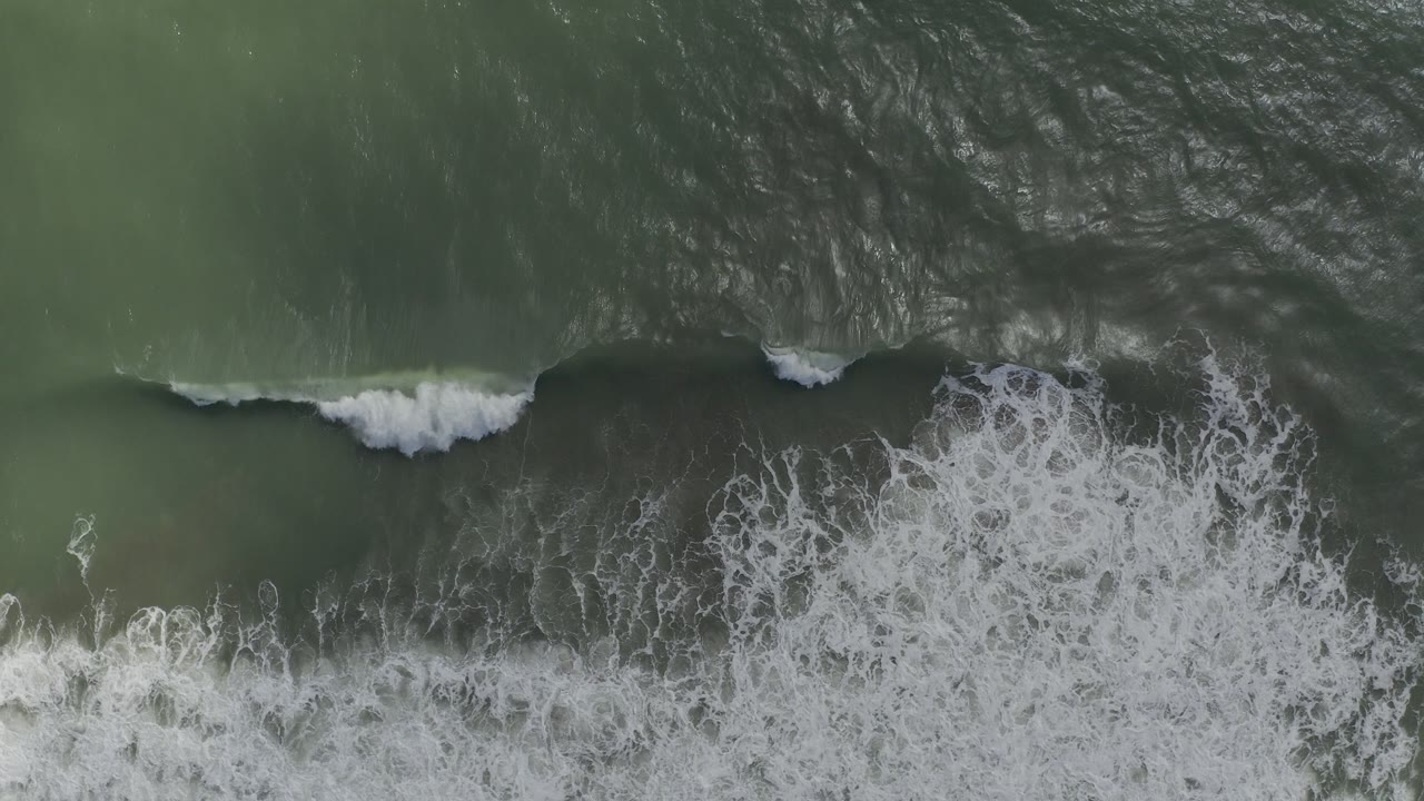 Top-down view of green-blue ocean swells in Los Cabos, Mexico, with a white foam break crossing the lower frame and no visible people.