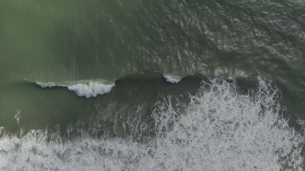 A dark band of rolling water cuts across the Los Cabos ocean surface while white foam gathers near the lower edge, with no visible people.