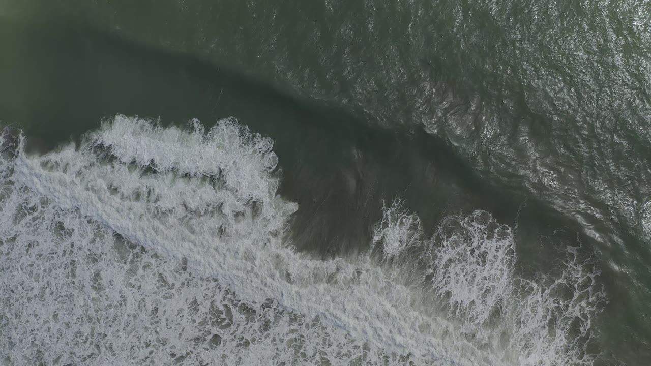 Overhead Los Cabos, Mexico frame with a broad white breaking wave pushing across green water and no visible people.
