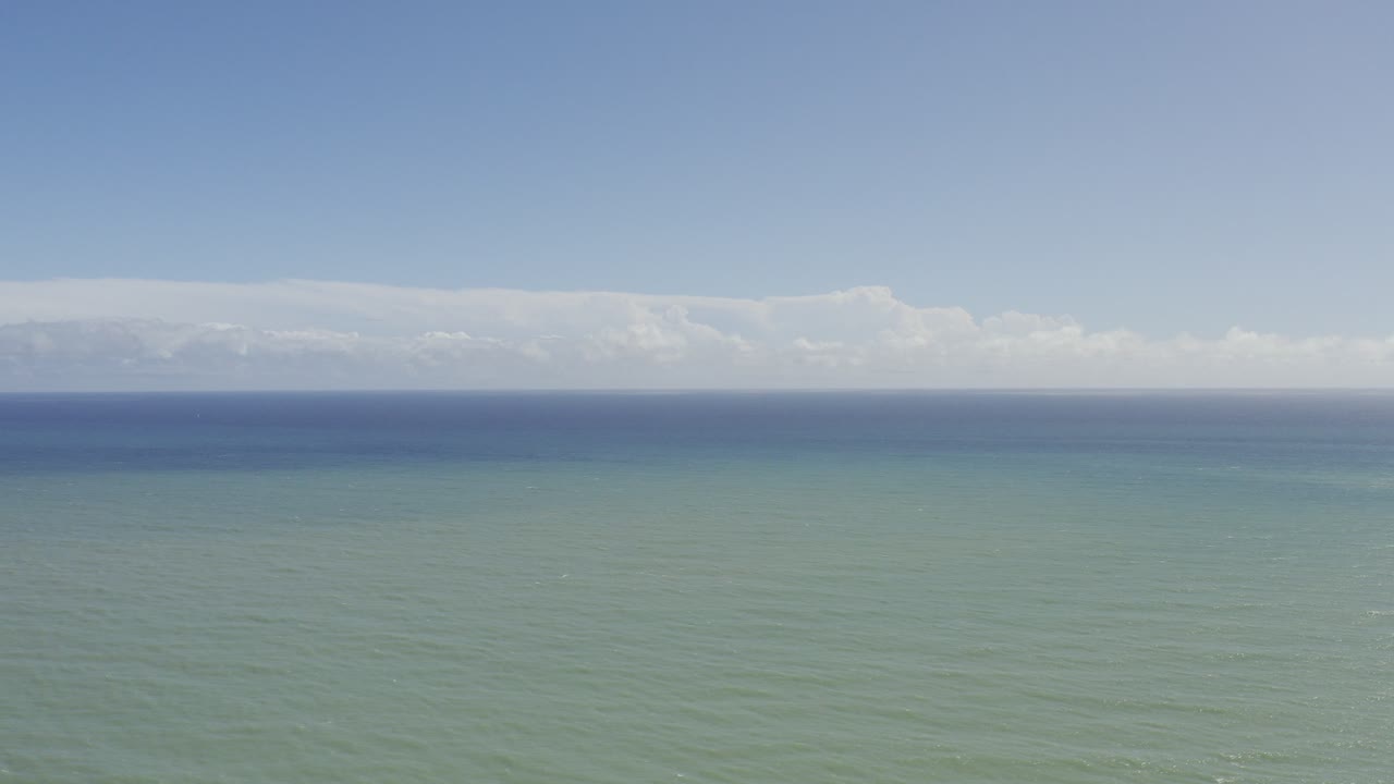 Los Cabos, Mexico ocean view with green water in the foreground, a blue horizon band, pale clouds, and no visible people.