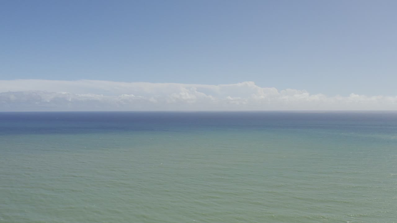 Los Cabos, Mexico seascape with the horizon held high, muted green water across most of the frame, distant clouds, and no visible people.