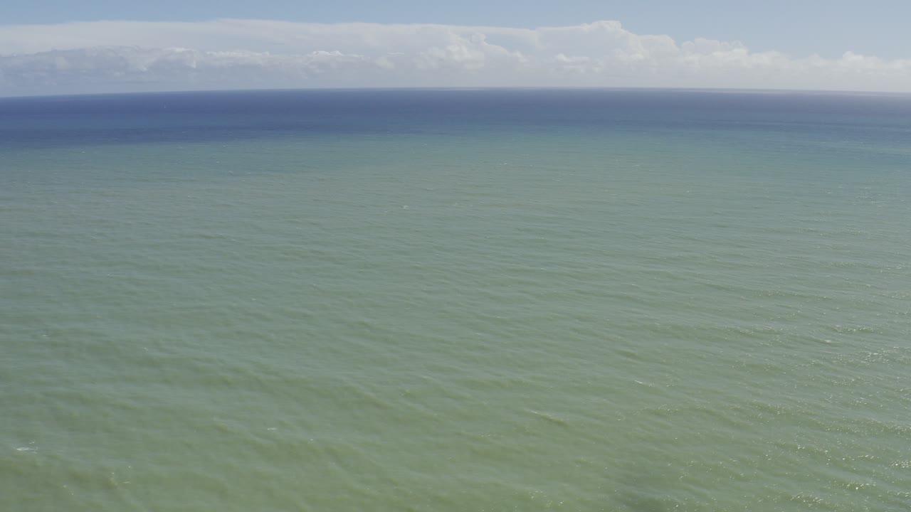 Sunlit ocean surface with horizon and clouds.