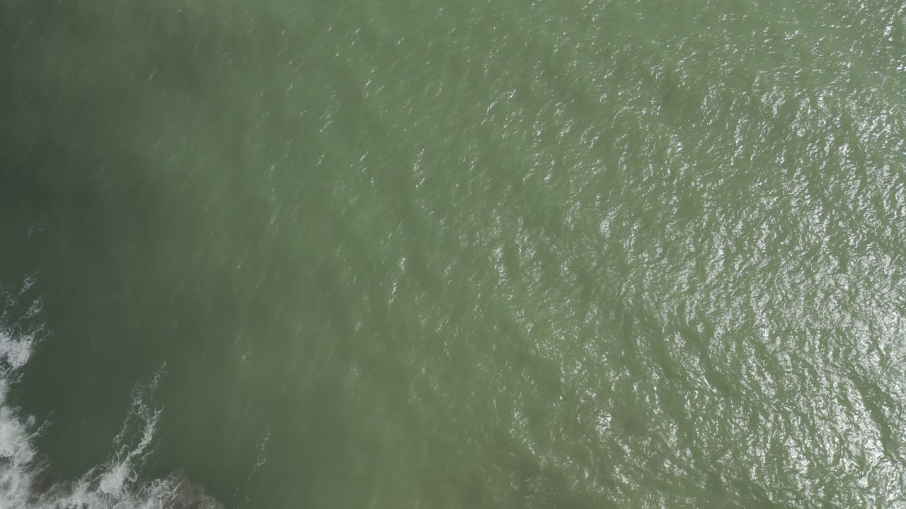 Top-down green ocean water with small white surf foam at the lower left edge.