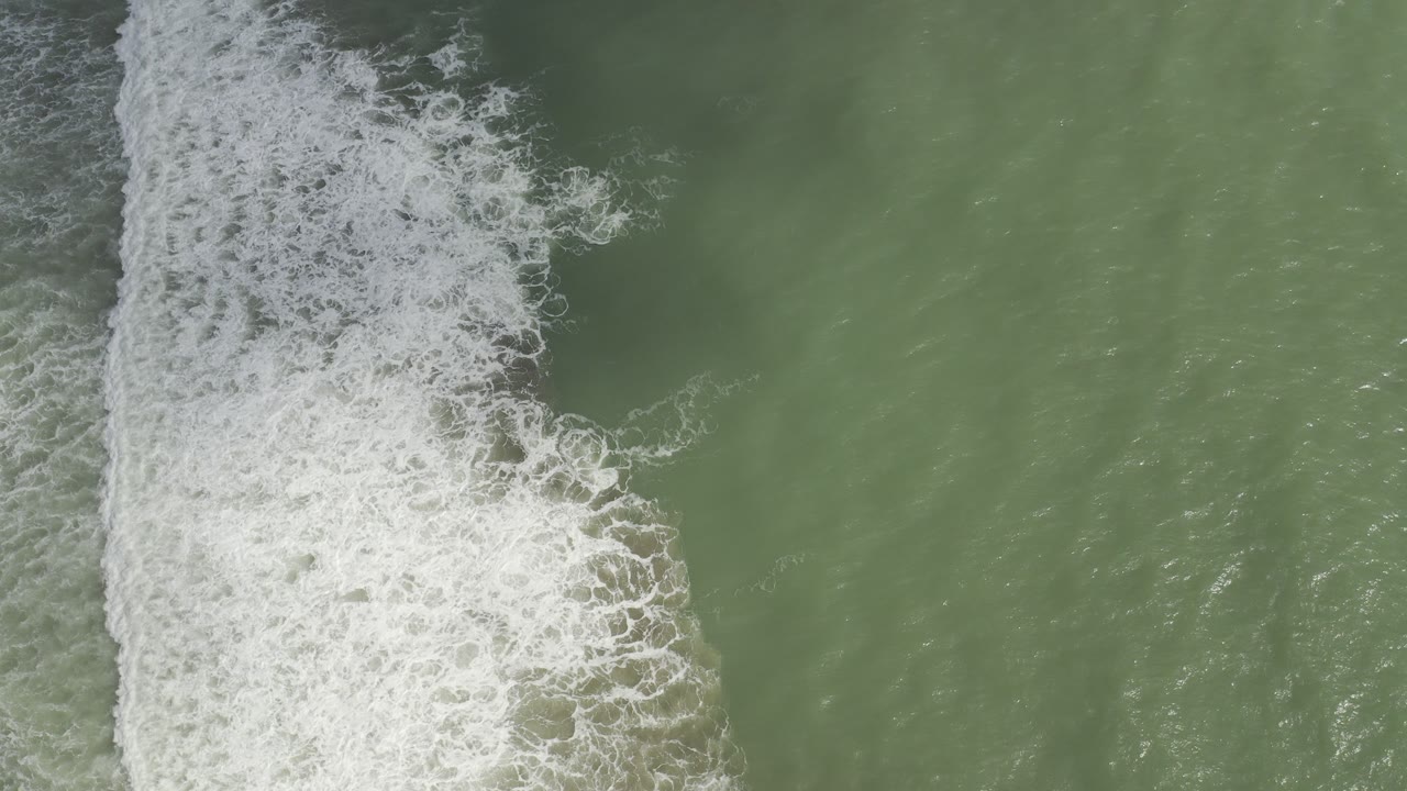 Overhead view of white surf foam running down the left side of green ocean water in Los Cabos, Mexico, with no visible people.