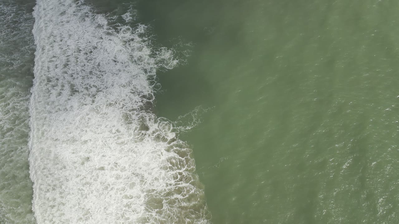 A vertical edge of white bubbled wave foam spreads across the left half of green sea in Los Cabos, Mexico, with no visible people.