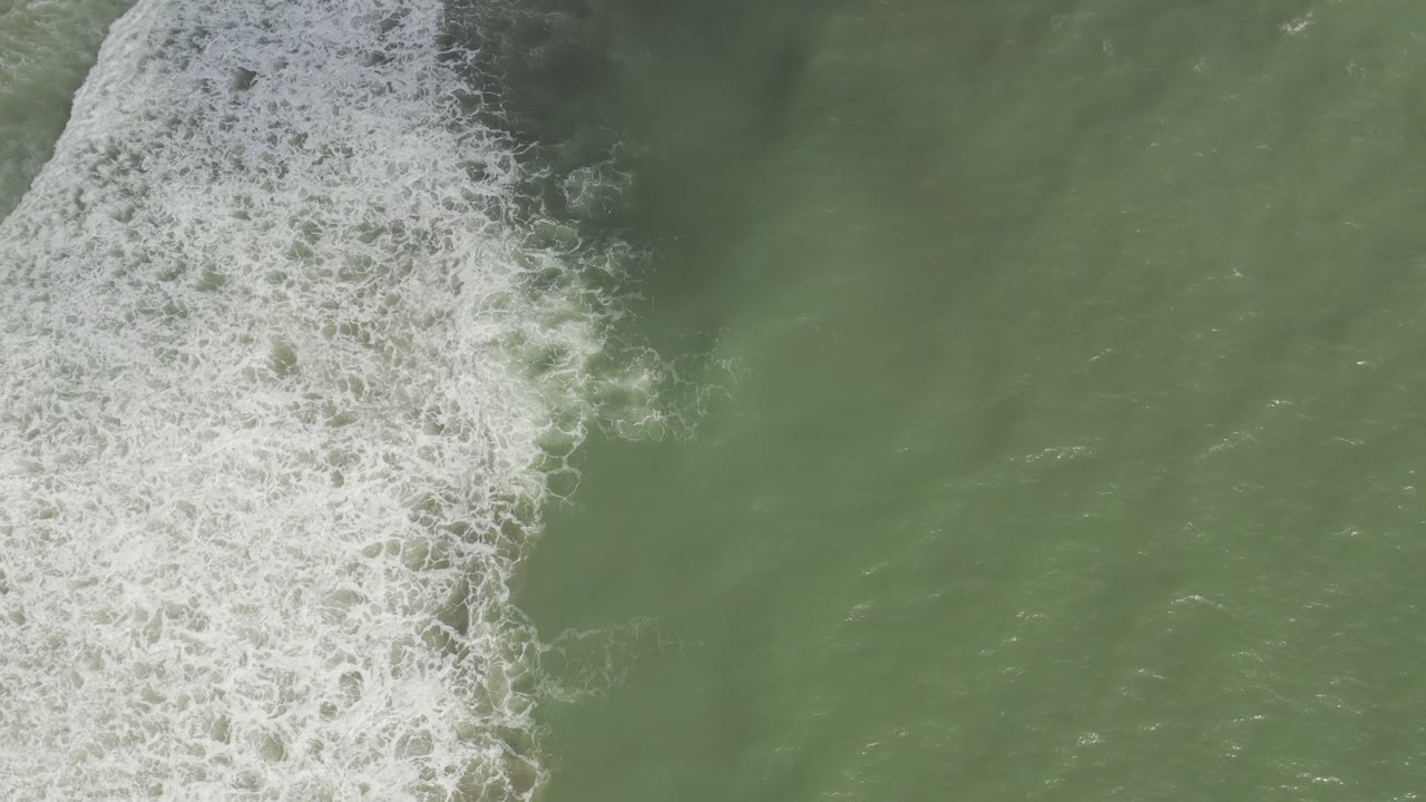Overhead view of green water in Los Cabos, Mexico, with white surf foam entering from the left side and no visible people.