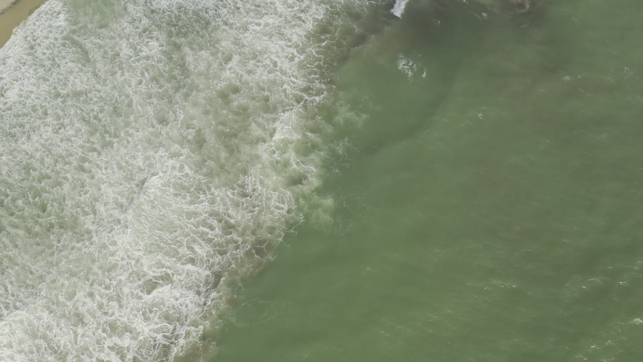 White foam line over green sea with a small sandy edge visible.