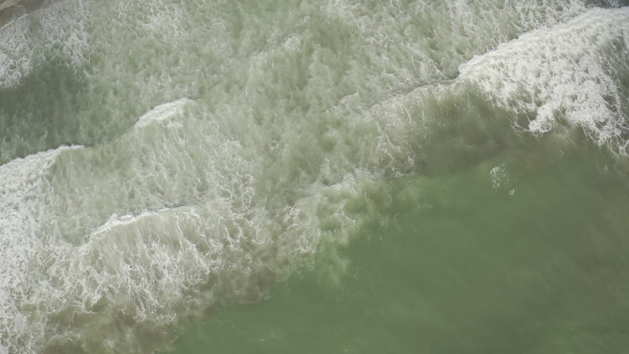 Top-down view of green surf and white breaking waves along the Los Cabos shore, with no visible people.