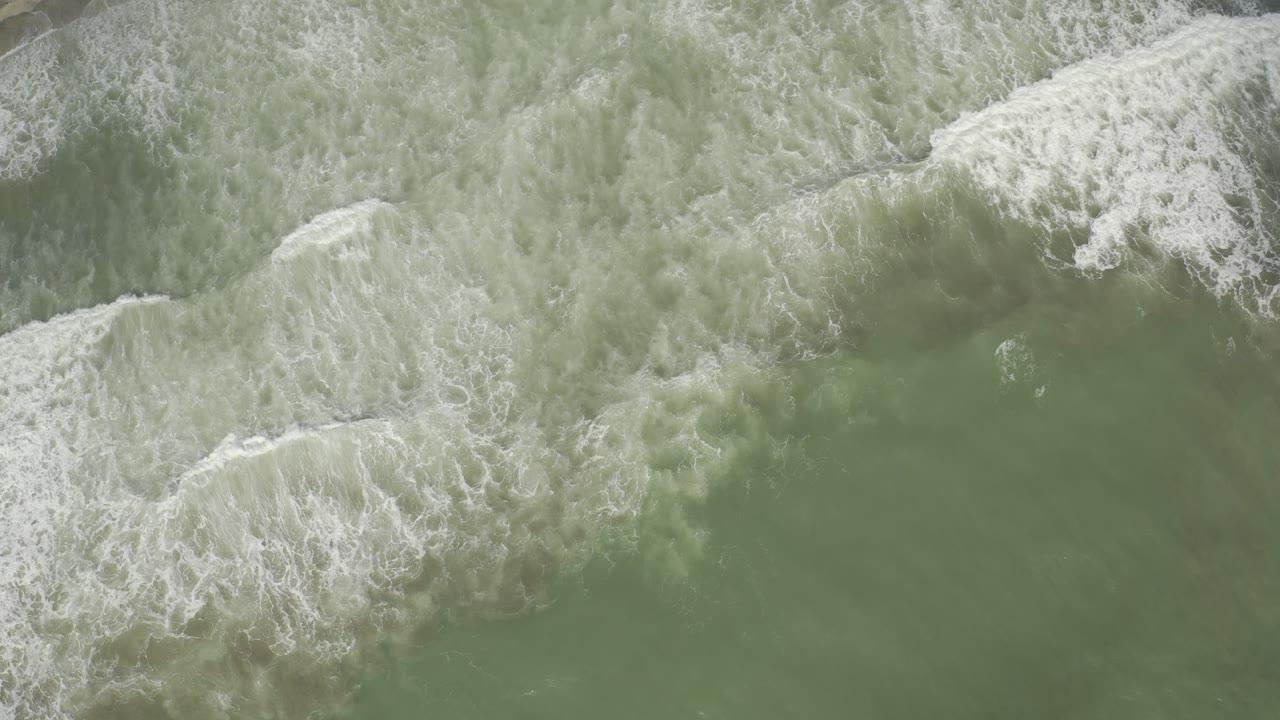 Aerial frame of white foam folding diagonally across green ocean water in Los Cabos, with no visible people.