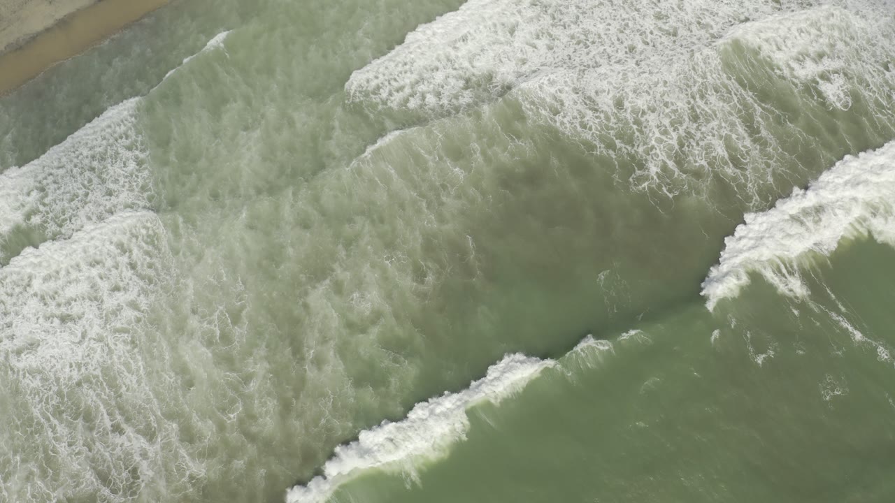 Diagonal bands of surf and green seawater viewed from overhead.