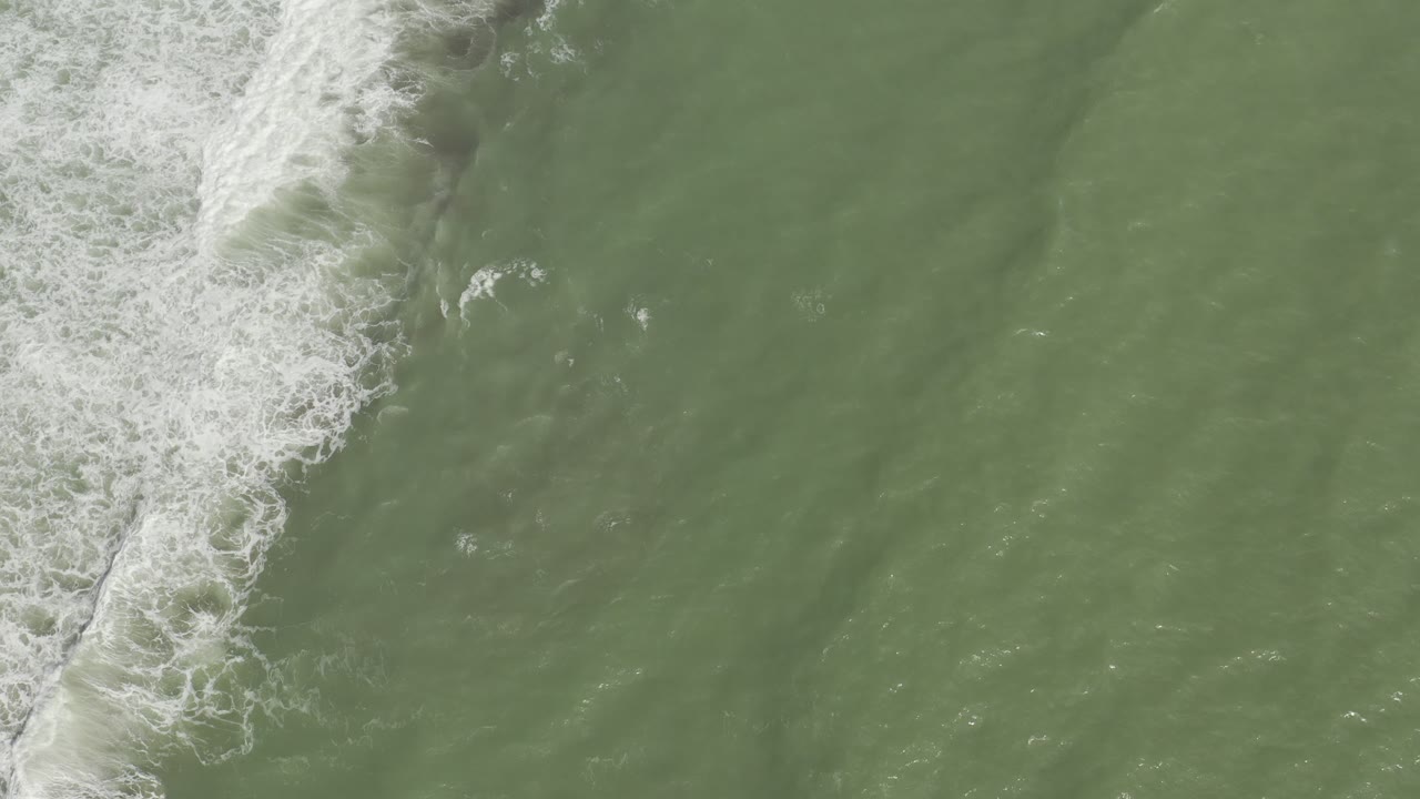 Overhead ocean view with a diagonal white surf line and muted green water.