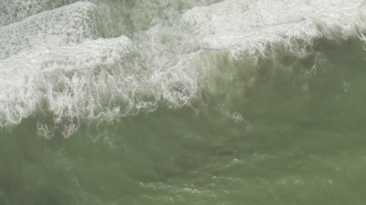 Top-down Los Cabos ocean frame with several white wave bands moving through green sea water and no visible people.