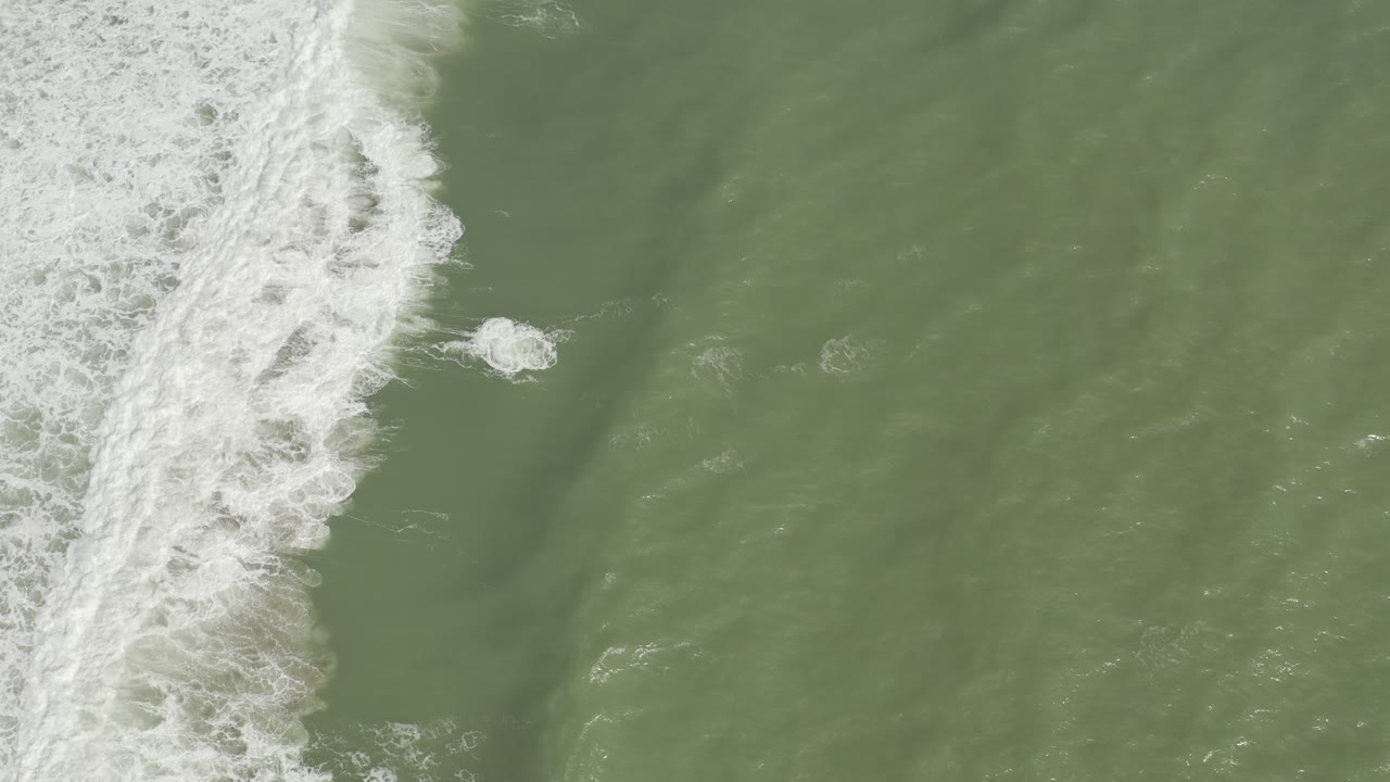 Narrow white surf band over muted green ocean water.