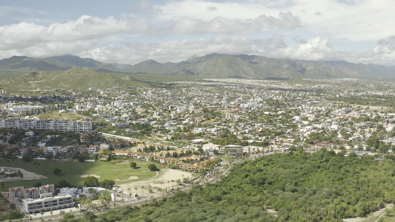 Aerial view over green hillside, golf course, town buildings, and distant mountains.
