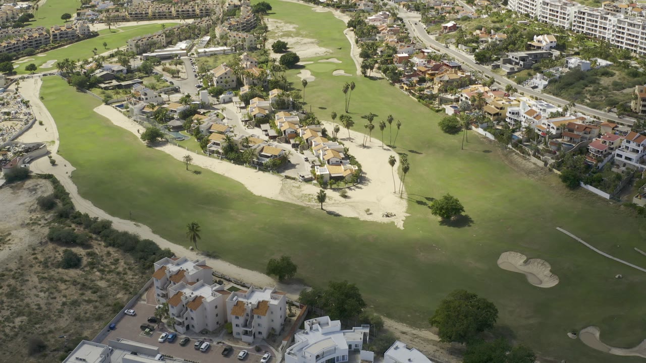 A slightly shifted Los Cabos aerial shows a broad fairway, pale sand traps, residential roofs, curving roads, and no visible people.