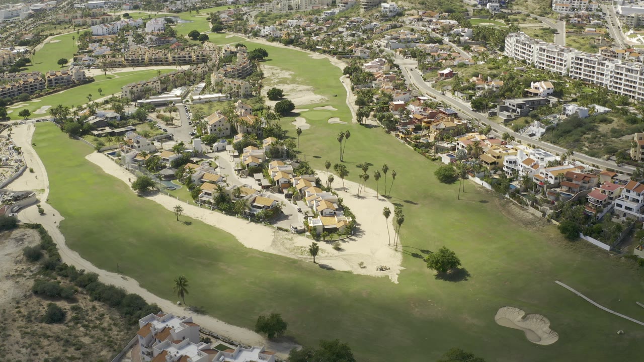 Aerial view of homes beside a golf course with larger buildings beyond.