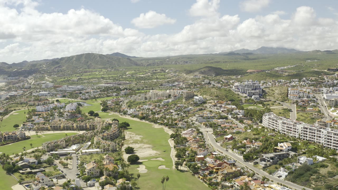 Aerial neighborhood view with golf greens, white buildings, roads, and distant hills.
