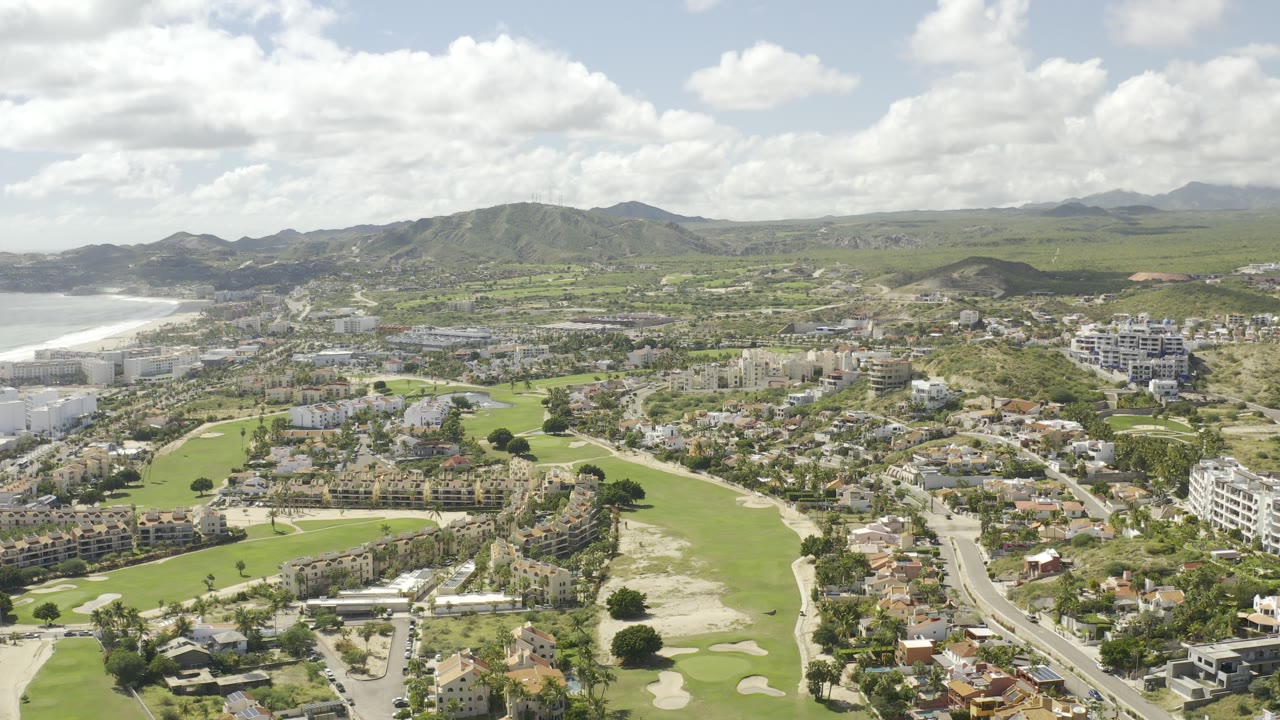 Aerial view of golf-course greens, homes, coast, and mountains.