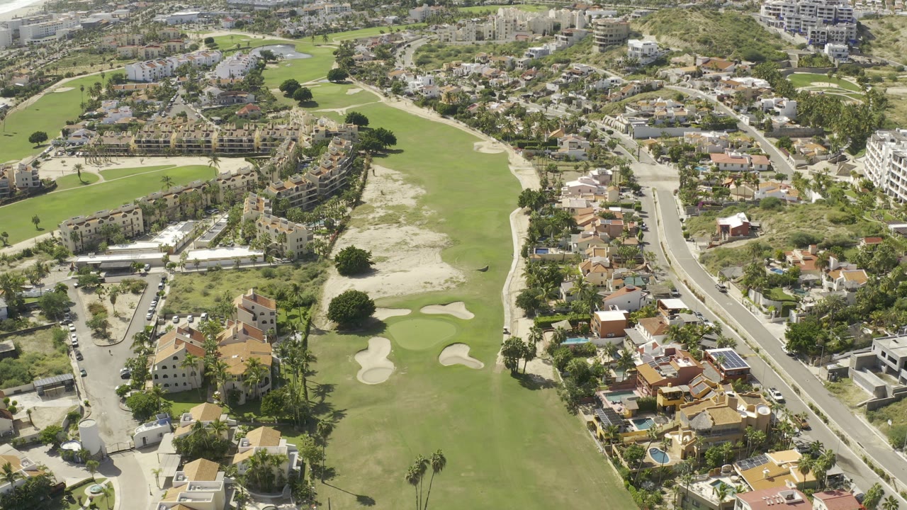 Aerial Los Cabos view with the fairway running vertically through the frame, a curved road beside clustered houses, and no discernible faces.
