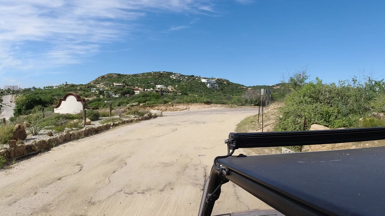 Dirt road and desert hills seen past a dark vehicle edge.