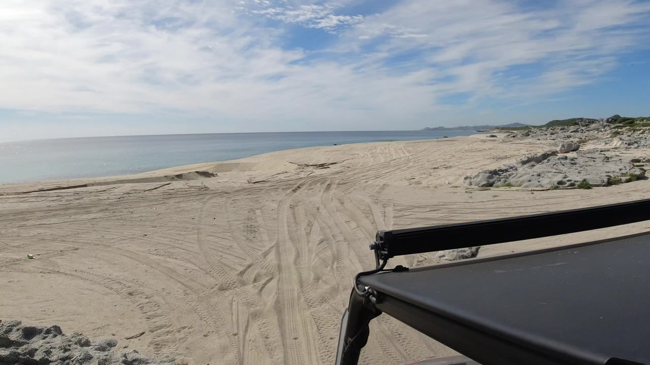 Jeep foreground on sandy beach tracks beside the sea.