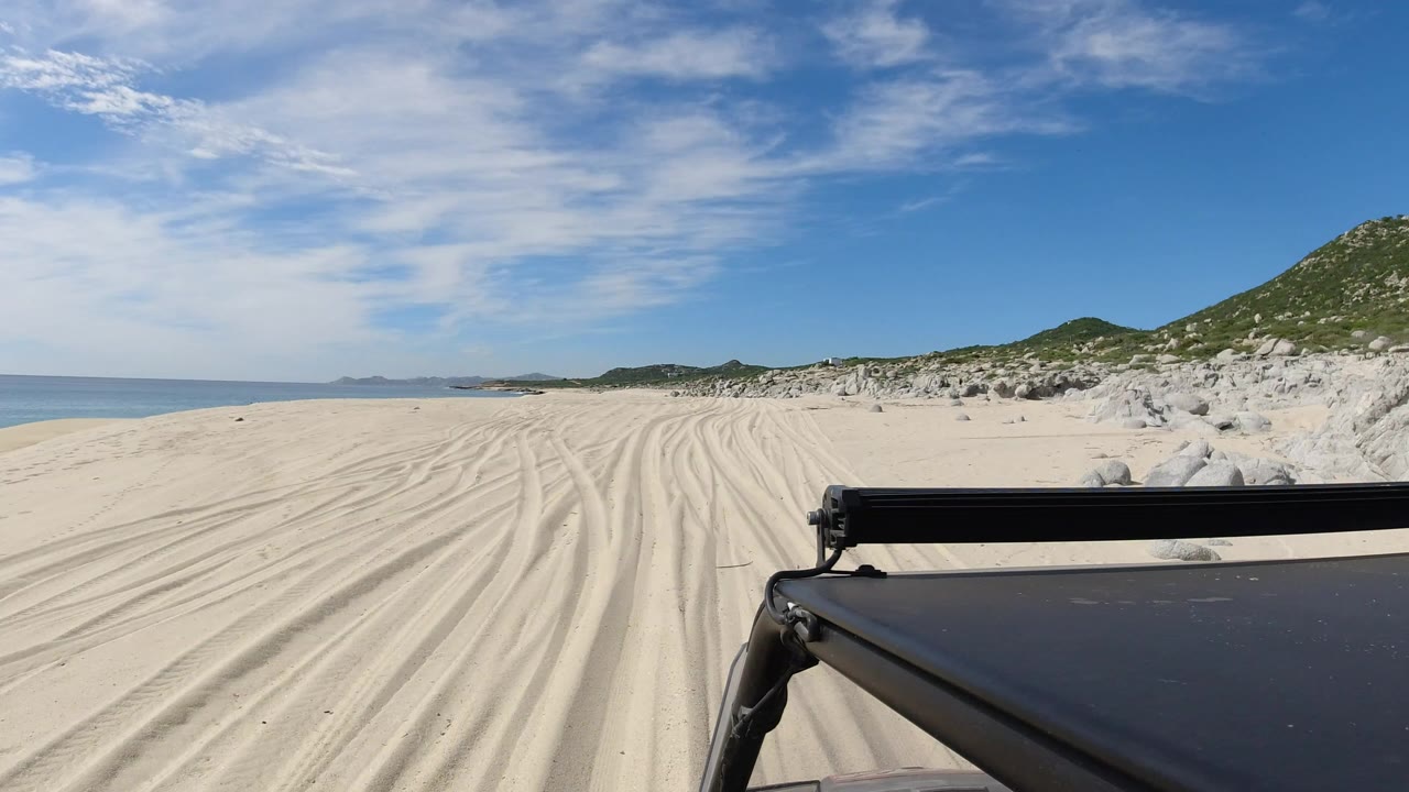 Truck foreground on sandy beach tracks beside sea and dunes.