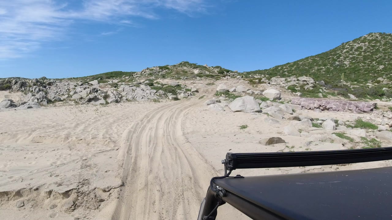 Sandy track through rocks and low hills under blue sky