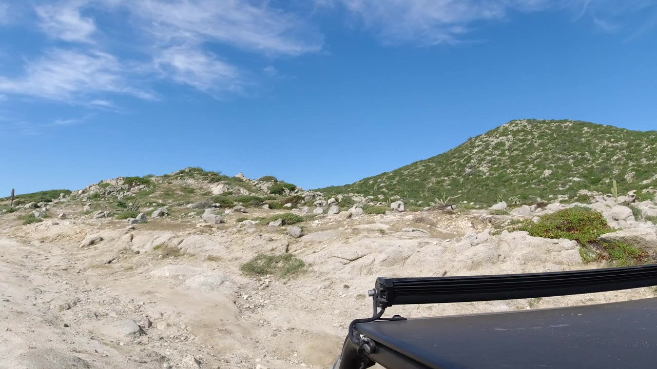 Black SUV roof on a rocky dirt road below a green hillside.