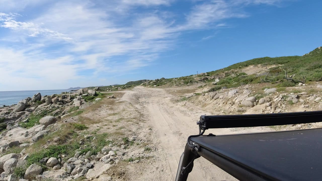 Dirt road beside coastal rocks with car roof in foreground