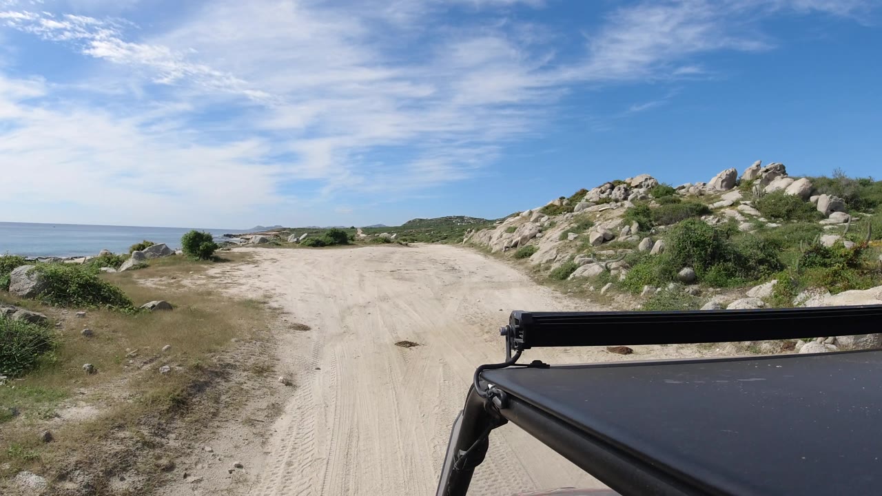 Unpaved road between ocean on the left and rocky hillside on the right.
