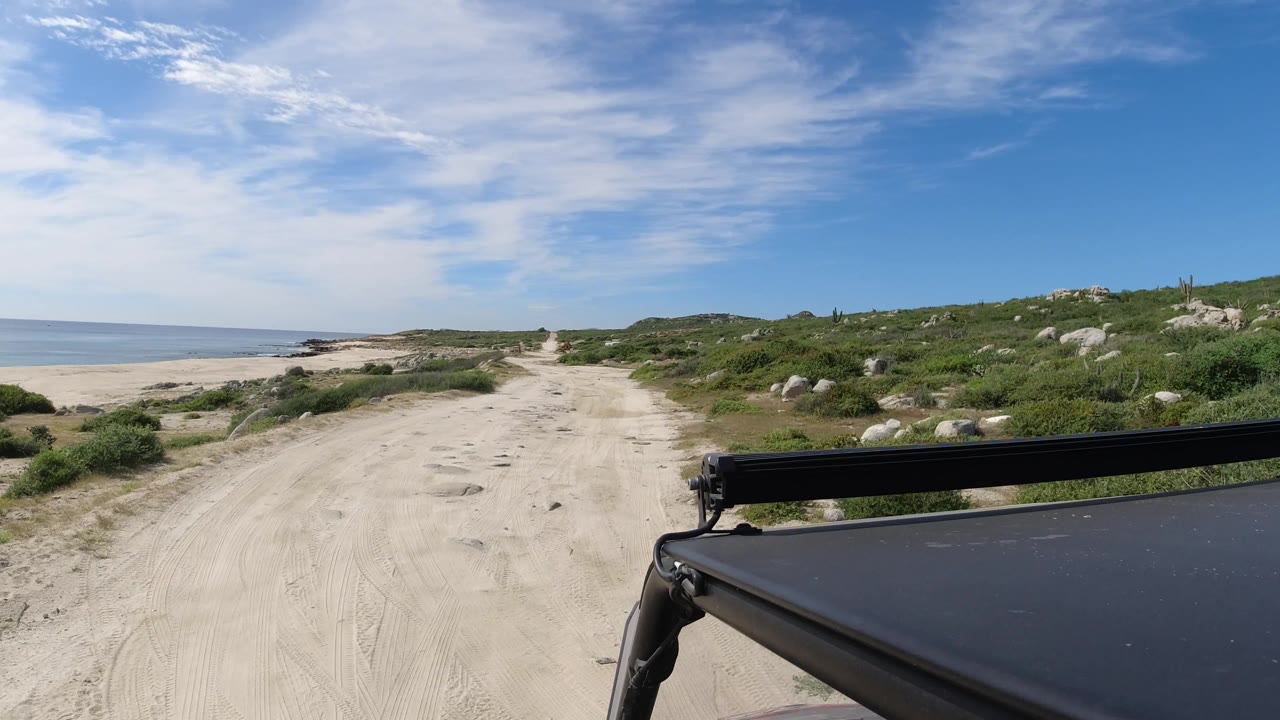Wide beach road view with more shoreline and ocean exposed on the left.