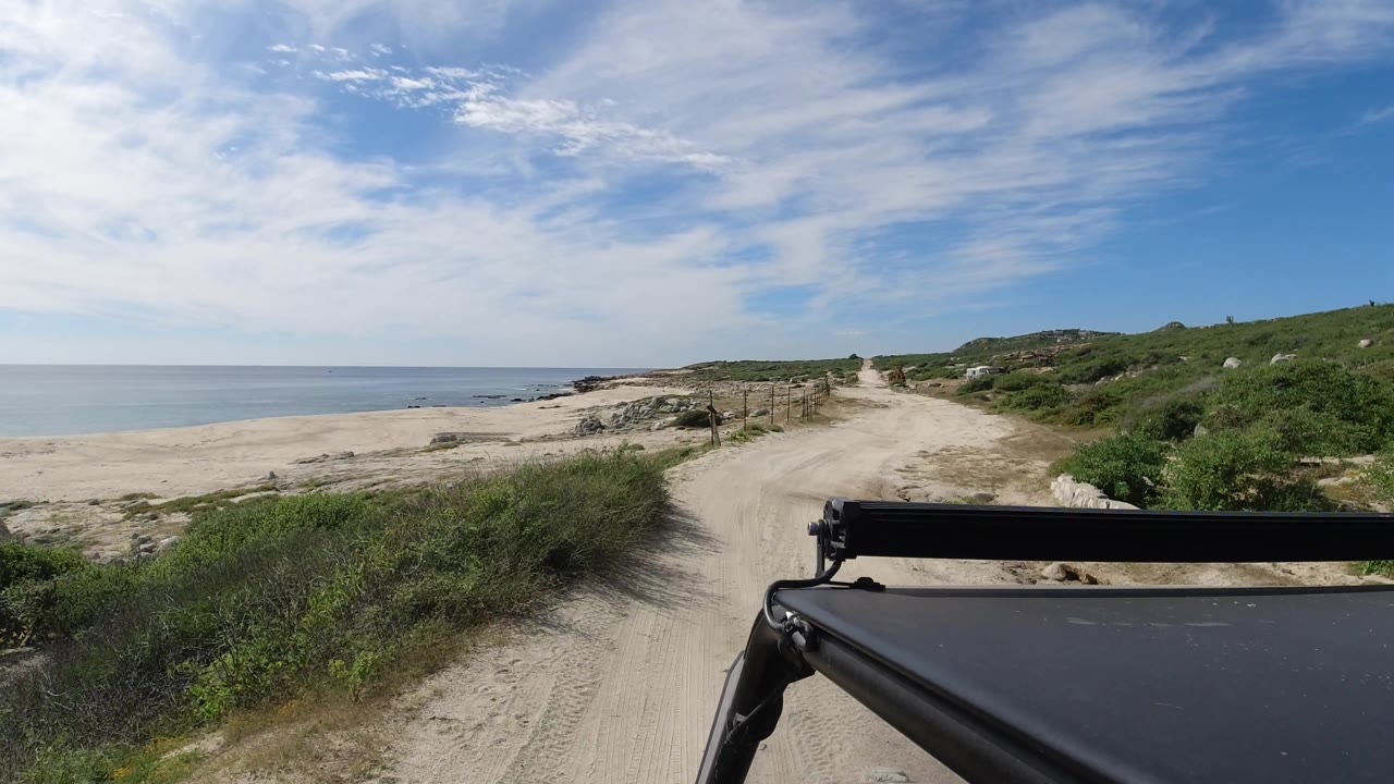 Coastal dirt road with fence posts and ocean beside it