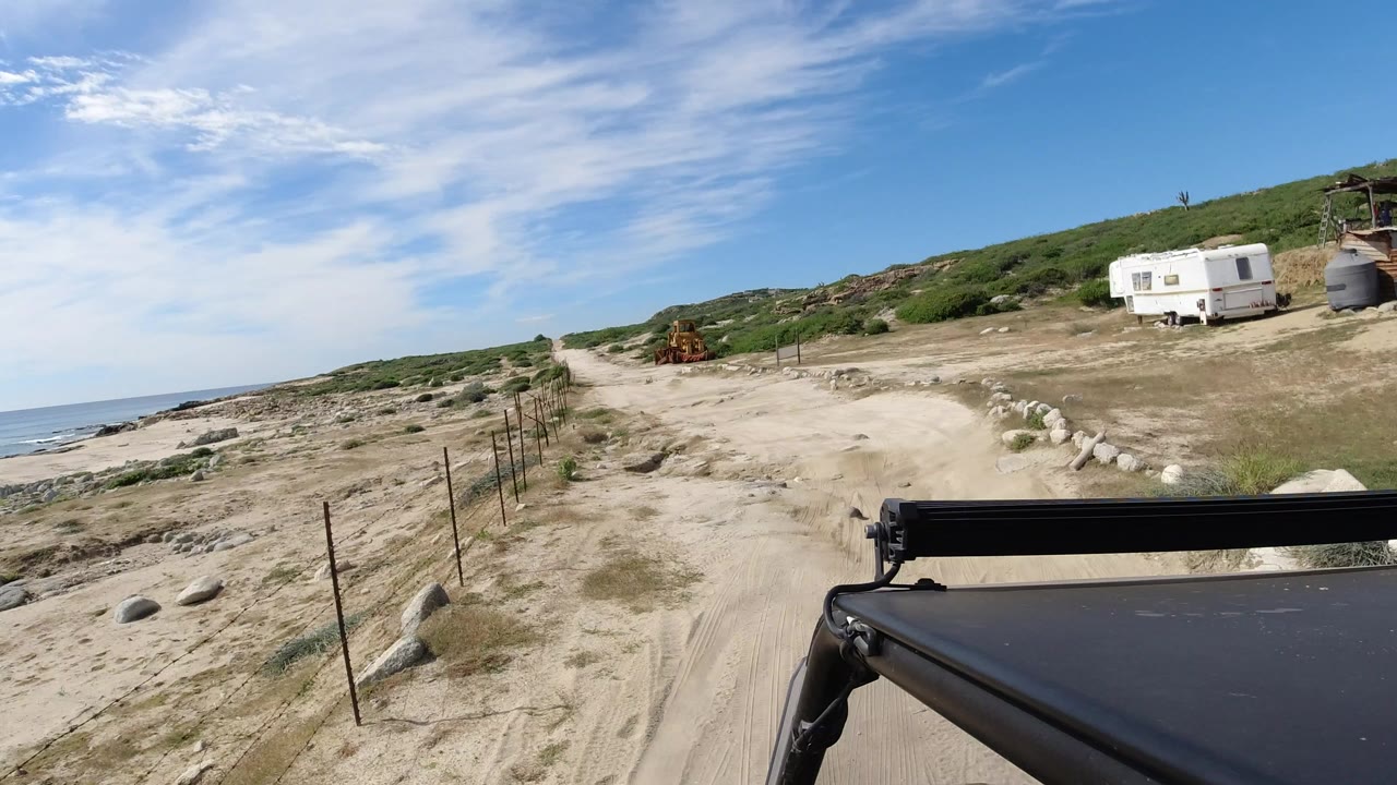 Sandy coastal road viewed over a vehicle roof near the ocean.