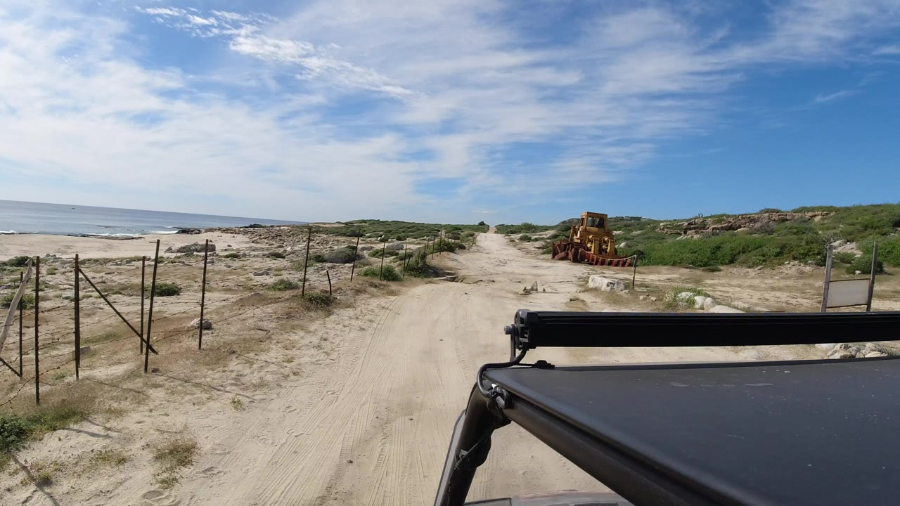 Sandy beach road with ocean, fencing, and Jeep roof foreground.