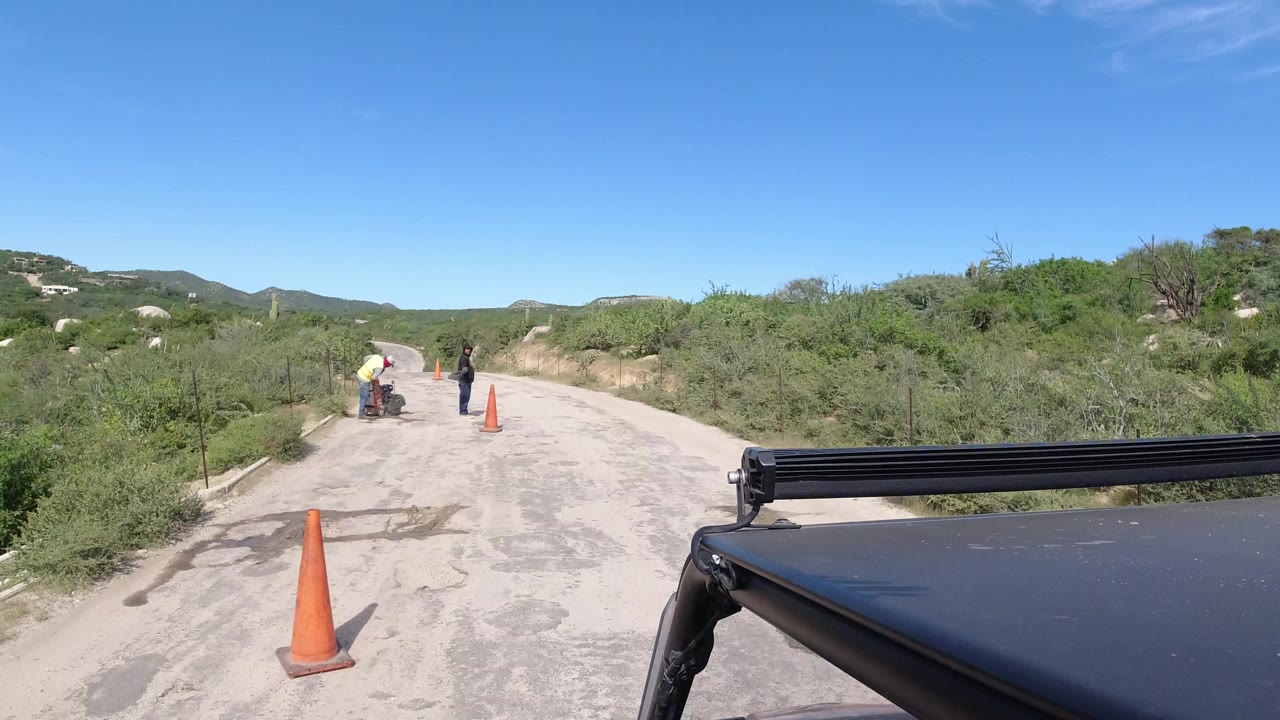 Safari vehicle view of a road with workers and traffic cones ahead.