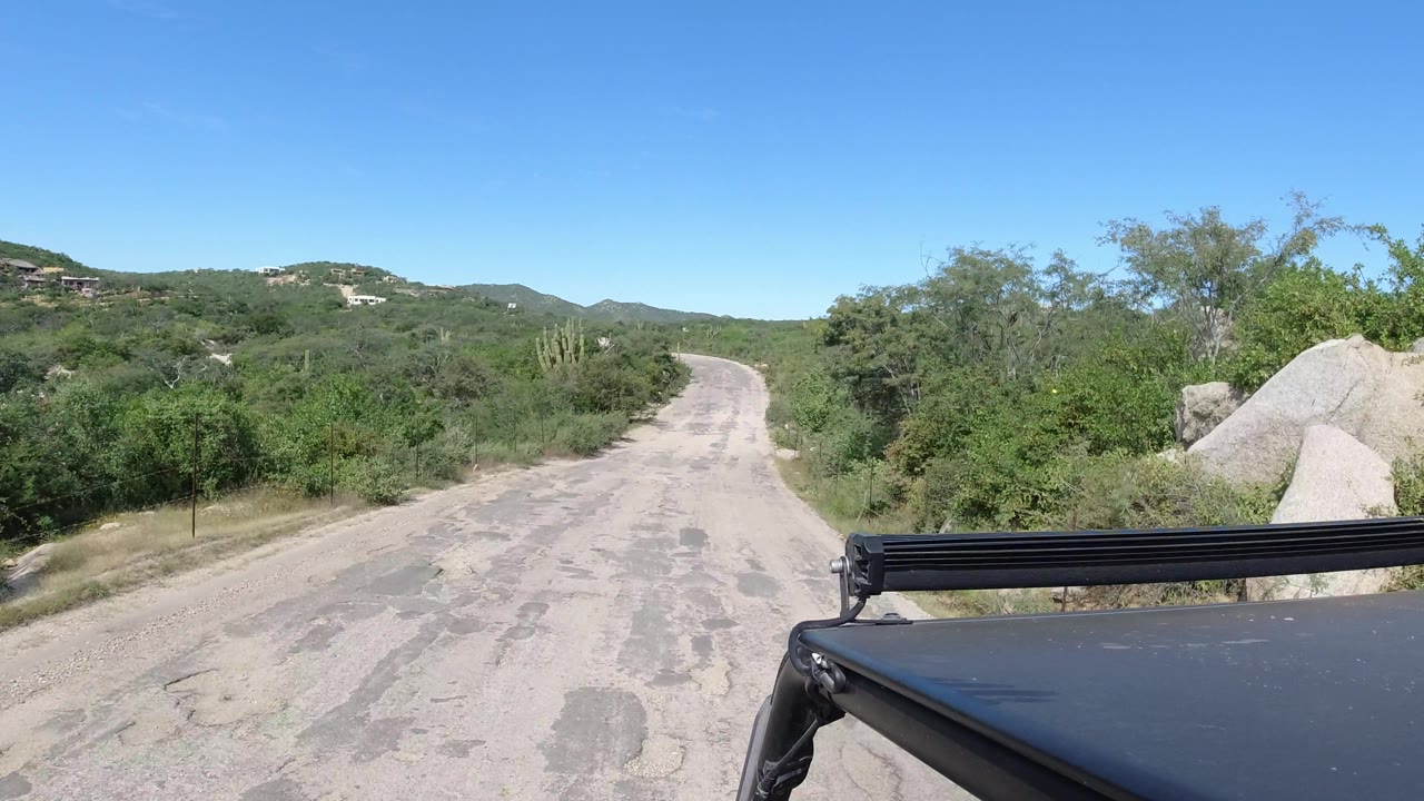 Patched dirt road bordered by desert plants and boulders from a vehicle view.