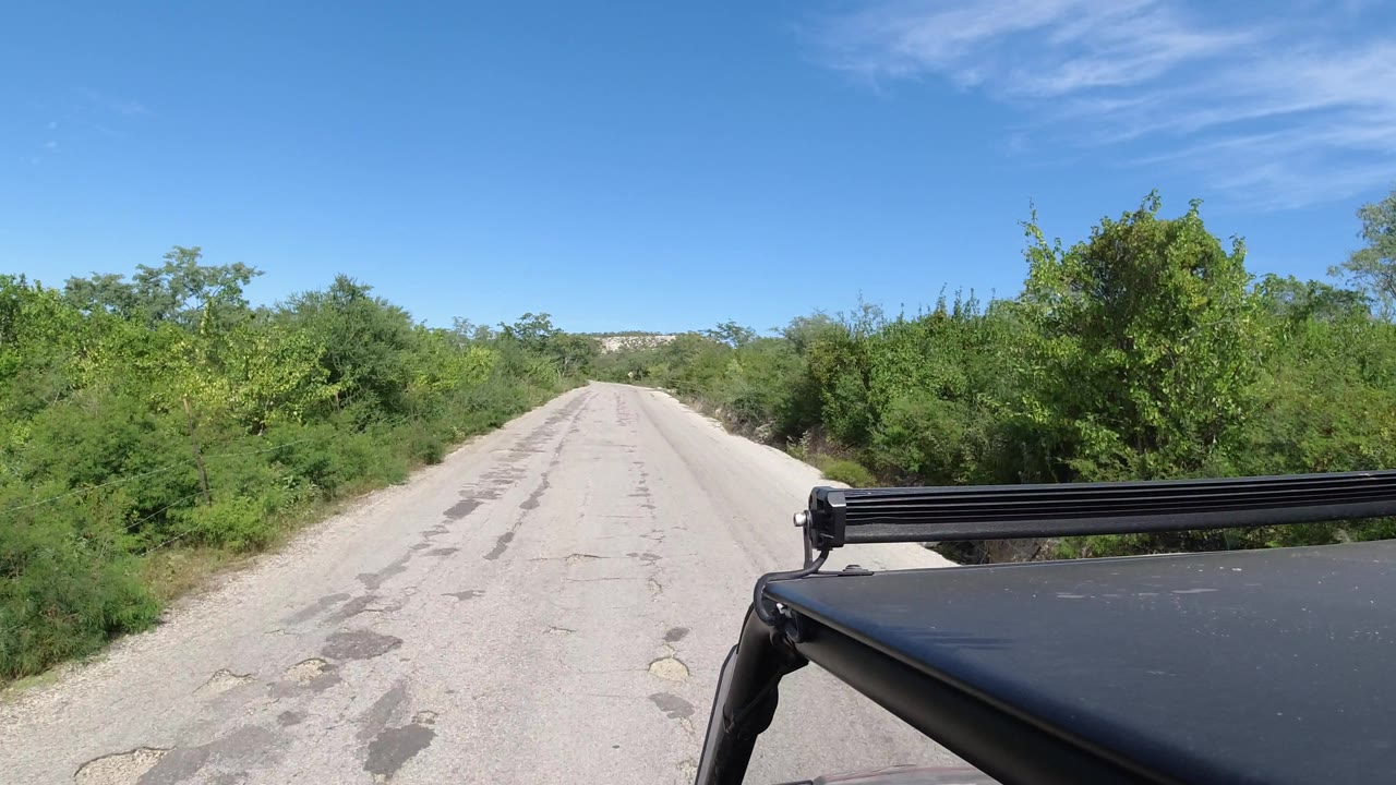 Sandy road with heavier greenery on the right and Jeep roof in frame.