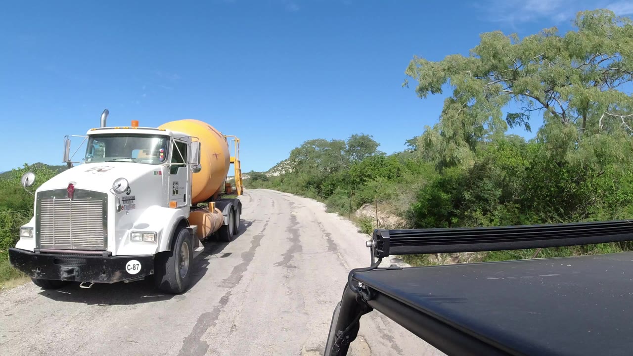 White cement mixer truck beside a black car on a sunny road