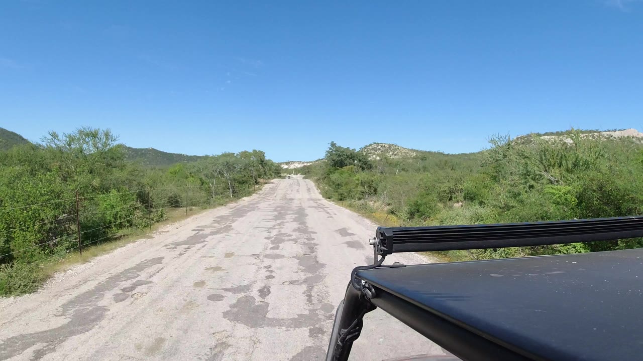 Paved road through green countryside with vehicle roof in foreground.