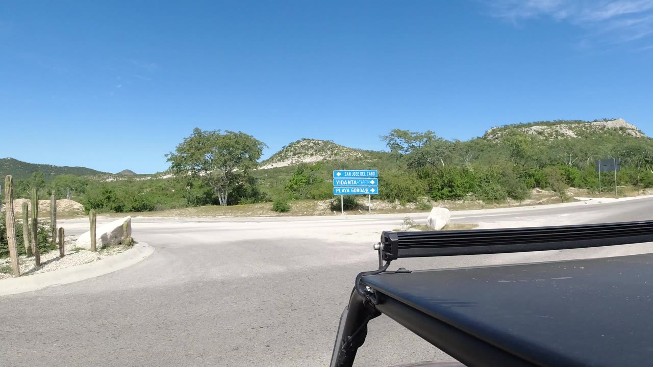 Paved road junction with blue signs, green hills, and vehicle roof edge.