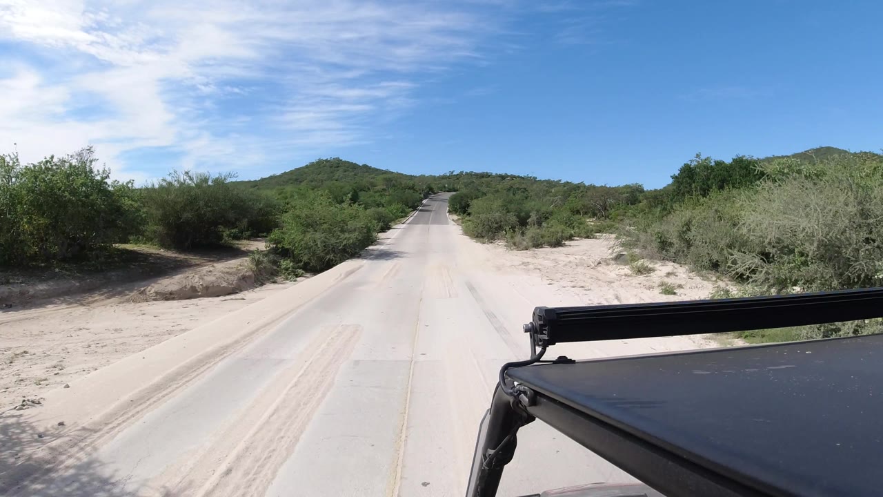 Road with sandy shoulders and black vehicle rail at lower right