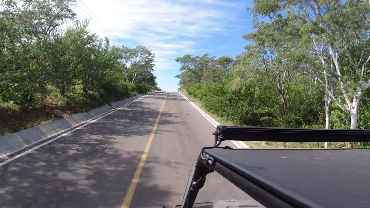 Two-lane road ahead with trees and vehicle roof rack in foreground.