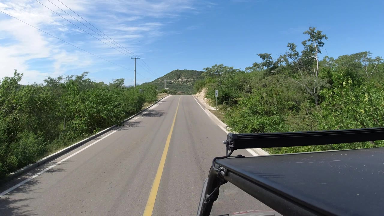 Road curves gently past trees and brush toward low hills.