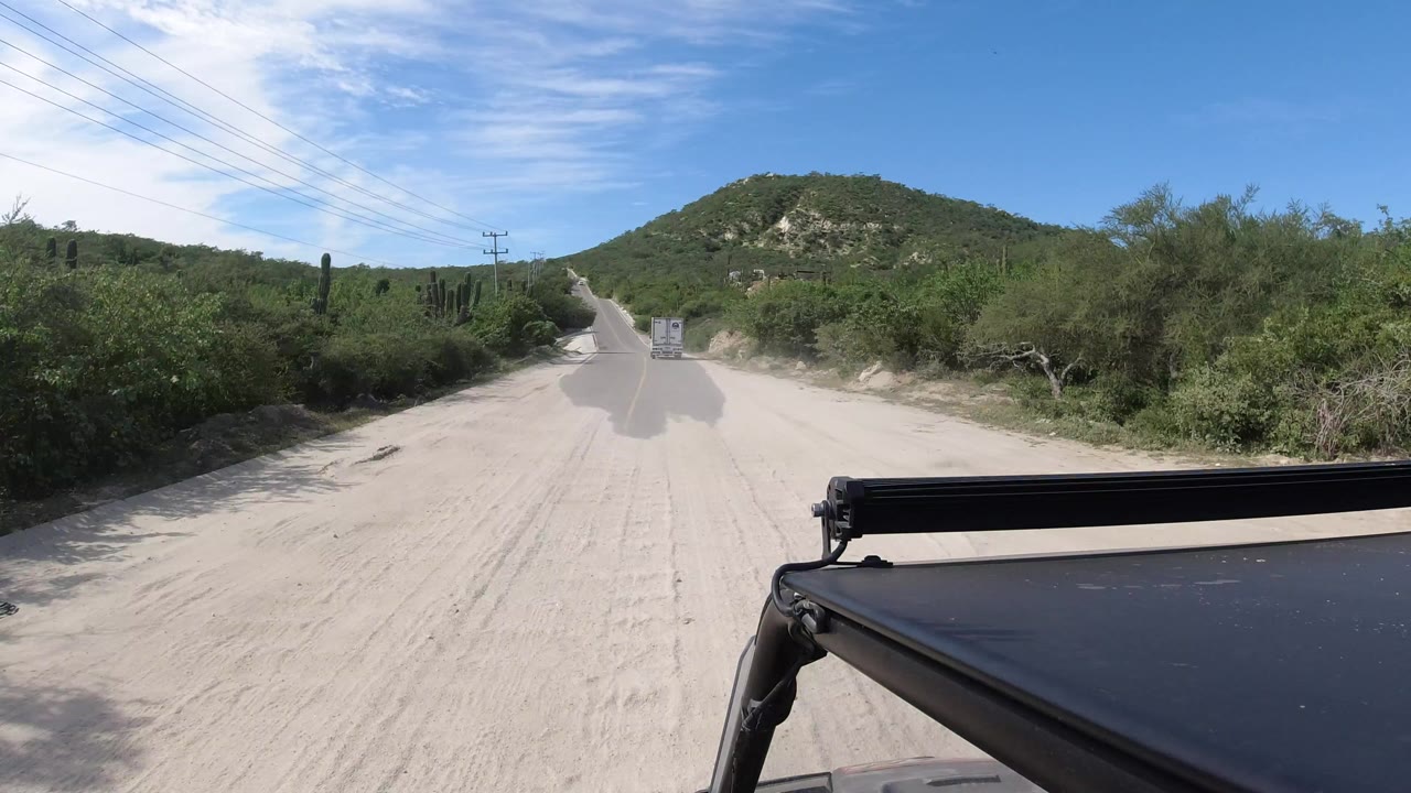Desert road shoulder with vehicle roof rail and hill ahead.