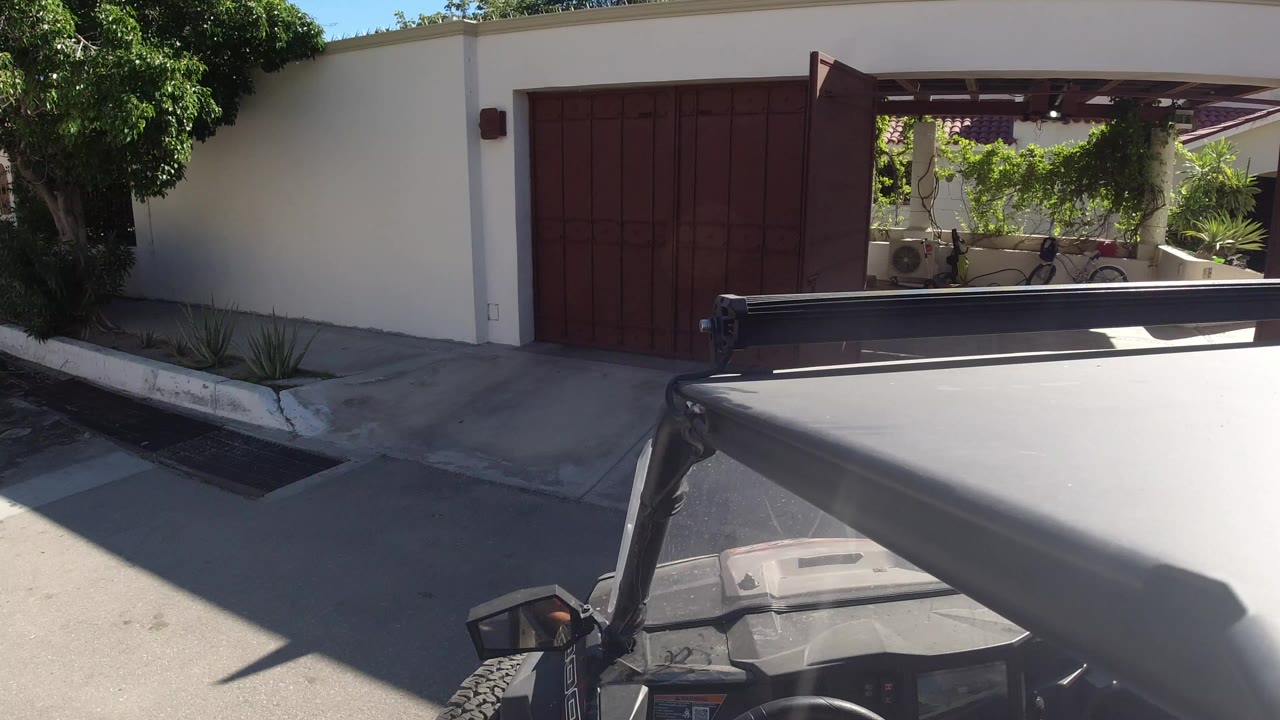 Red-brown driveway gate beside a white wall seen over an off-road vehicle roof.