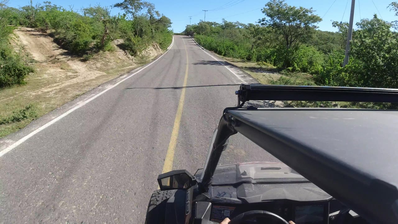 Road curving past a sandy dirt entrance and green vegetation.