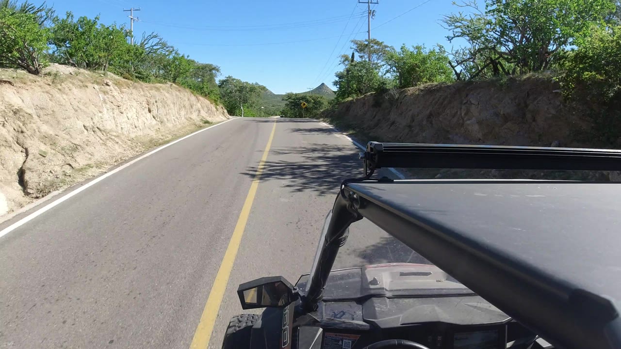 Forward road view with vehicle hardware in the foreground and a curve warning sign ahead.