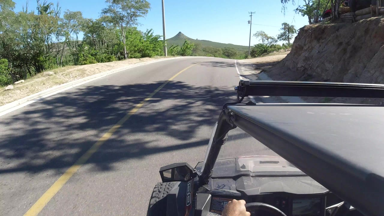 Open vehicle driving on a paved road lined with trees and hillside shade.