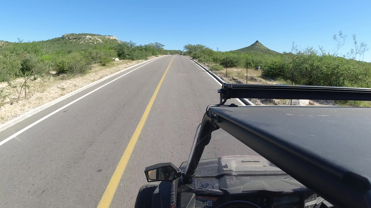 Straight paved road with desert brush and vehicle frame.